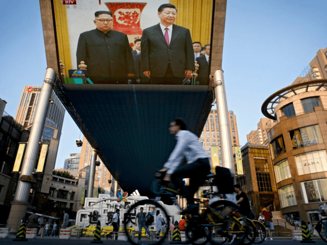 People bicycle past a giant TV screen broadcasting the meeting of visiting North Korean le