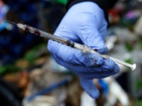 In this Nov. 8, 2017 photo, Steph Gaspar, a volunteer outreach worker with The Hand Up Project, an addiction and homeless advocacy group, holds a used and blood-filled needle used for drug injection that she found while cleaning up a homeless encampment in Everett, Wash. Gaspar said used needles like …