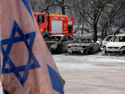 An Israeli flag is pictured in front of vehicles that were badly damaged by a fire amidst