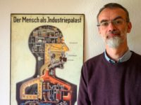Department head at the Institute of Anatomy of the Brandenburg Medical School (MHB) Andreas Winkelmann poses next to a poster from 1926 detailing the human body as an "Industry Palace", in his office in Neuruppin on April 30, 2019. - More than seven decades after the end of World War …