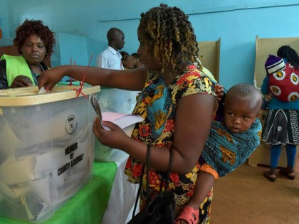A woman carrying a baby on her back casts her ballot at a polling station in Gatundu South