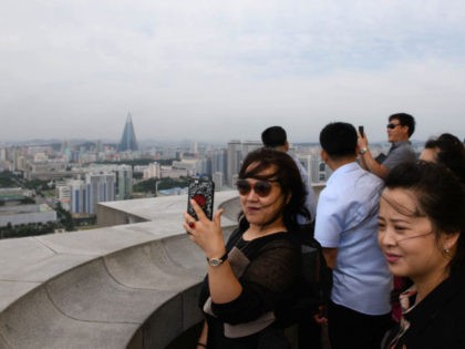 Tourists take photos from a viewing deck of the Juche tower in front of the city skyline o