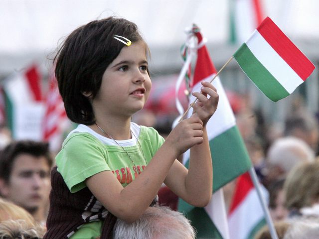 Budapest, HUNGARY: Sitting on his father's back, a girl waves a national flag on Koss