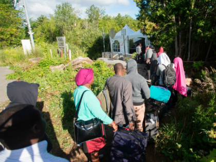 TOPSHOT - A long line of asylum seekers wait to illegally cross the Canada/US border near Champlain, New York on August 6, 2017. - In recent days the number of people illegally crossing the border has grown into the hundreds. (Photo by Geoff Robins / AFP) (Photo credit should read …