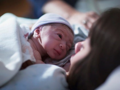 A newborn mixed race asian caucasian in a blue cap baby rest on his brunette asian mothers chest and stares into her eyes for the first time - stock photo