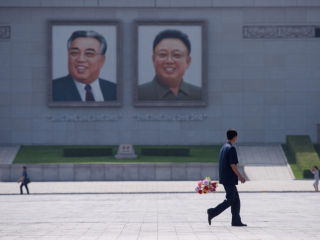 A man holding a bunch of flowers walks past the portraits of late North Korean leaders Kim Il Sung and Kim Jong Il, on Kim Il Sung square in Pyongyang on June 20, 2019, as Chinese President Xi Jinping visits the country. - Xi Jinping started a historic visit in …