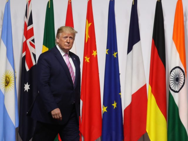 US President Donald Trump walks past G20 member flags as he is welcomed by Japanese Prime