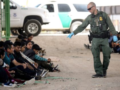 A U.S. Border Patrol agent gestures towards migrants being detained after crossing to the
