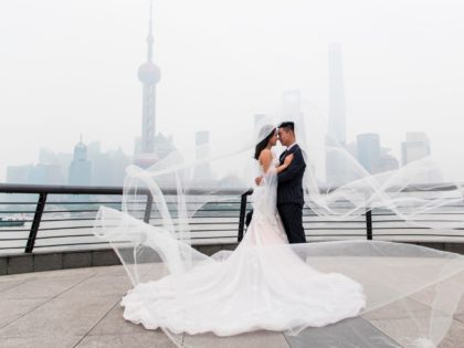 TOPSHOT - A couple poses for a wedding photograper at the promenade on the Bund along the Huangpu River, seen against the skyline of the Lujiazui Financial District in Shanghai on a hazy and polluted day on May 29, 2018. (Photo by Johannes EISELE / AFP) (Photo credit should read …