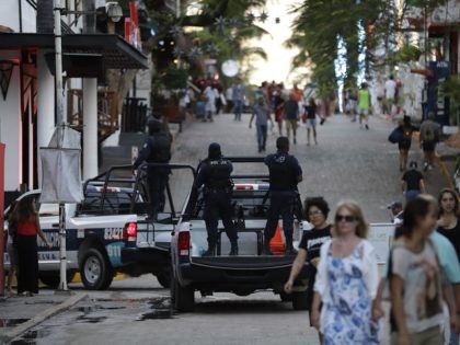 Municipal police trucks drive past strolling tourists, as they leave the Blue Parrot club, where several people were killed in early morning gunfire, in Playa del Carmen, Mexico, Monday, Jan. 16, 2017. Deadly gunfire broke out in the crowded beachfront nightclub throbbing with electronic music before dawn on Monday, setting …