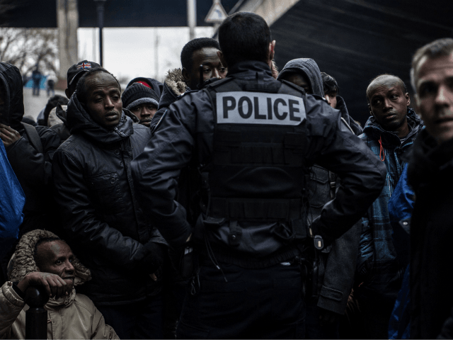 A policeman stand in front of Migrants waiting during the evacuation of a makeshift camp s