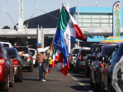 TIJUANA, MEXICO - MARCH 31: A man sells Mexican flags and other items as cars line up to cross into the United States at the San Ysidro Port of Entry, one of the busiest land border crossings in the world, on the U.S.-Mexico border on March 31, 2019 in Tijuana, …