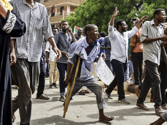 A Sudanese protester walking with a crutch joins others in a march during a mass demonstra