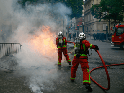 TOPSHOT - Firefighters extinguish a fire as protestors linked to the Yellow Vests (Gilets Jaunes) movement (unseen) take part in a demonstration on the side of the annual Bastille Day ceremony, on July 14, 2019, on the Champs-Elysees in Paris. (Photo by Abdulmonam EASSA / AFP) (Photo credit should read …
