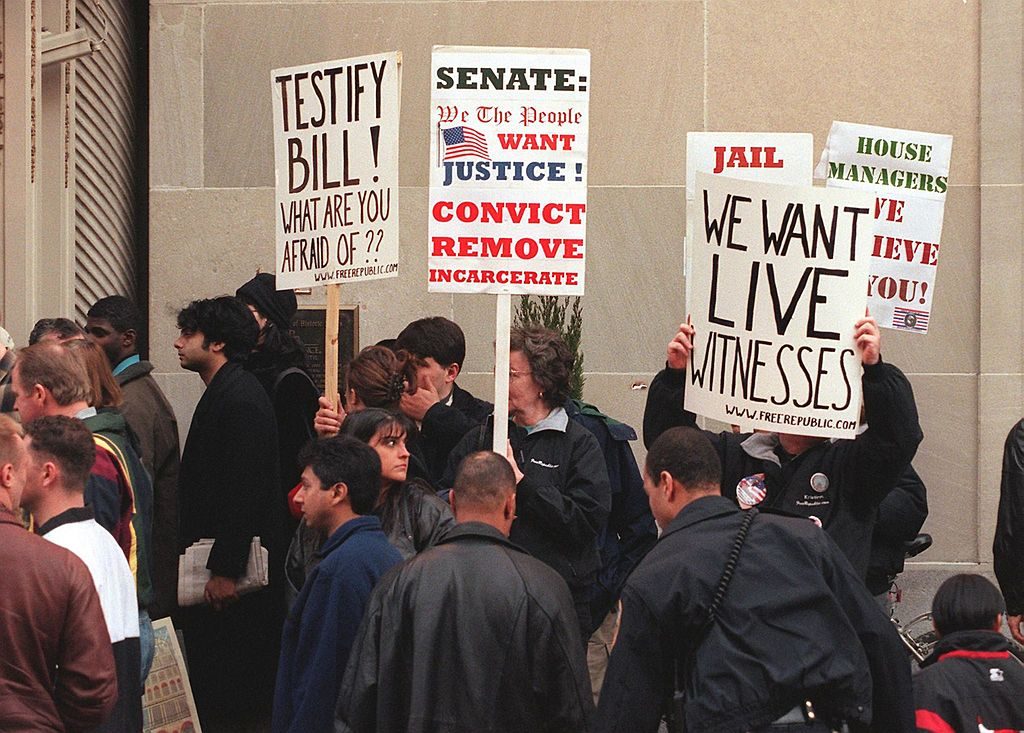 WASHINGTON, : Protesters demanding live witness testimony at US President Bill Clinton's impeachment trial and his removal from office wave posters in front of the Mayflower Hotel 30 January in Washington, DC, before the arrival of former White House intern Monica Lewinsky. Lewinsky is due to give a video taped deposition to Republican prosecutors 01 February which will be used in Clinton's impeachment trial before the Senate. AFP PHOTO/MARIO TAMA (Photo credit should read MARIO TAMA/AFP/Getty Images)