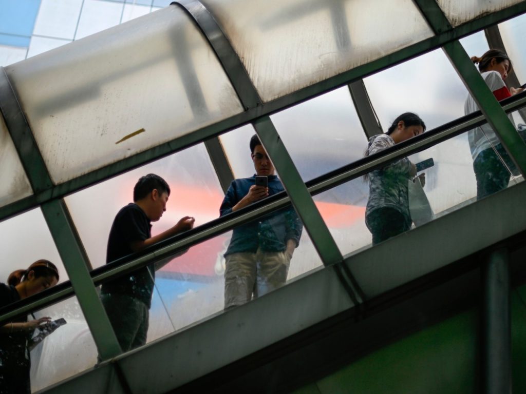 A group of pedestrians looks at their mobile phone as they ride an escalator to cross an overpass in Beijing on June 13, 2019. - Inflation in China rose to its highest level in more than a year in May driven by surges in pork and fruit prices caused by the African swine fever epidemic and bad weather, official data showed on on June 12. (Photo by WANG ZHAO / AFP) (Photo credit should read WANG ZHAO/AFP/Getty Images)