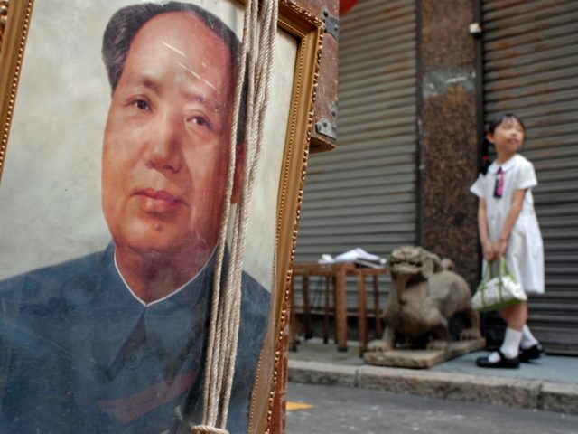 A schoolgirl stands on the pavement in front of a portrait of China’s revolutionary lead