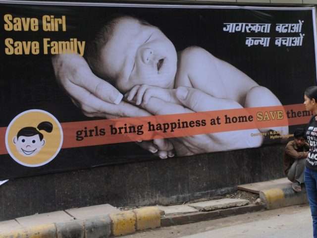 Young Indian women walk past a billboard in New Delhi on July 9, 2010, encouraging the birth of girls. Mostly as a result of sex-selective abortion, India is one of the few countries worldwide with an adverse child sex ratio in favour of boys. Under Indian law, tests to find …