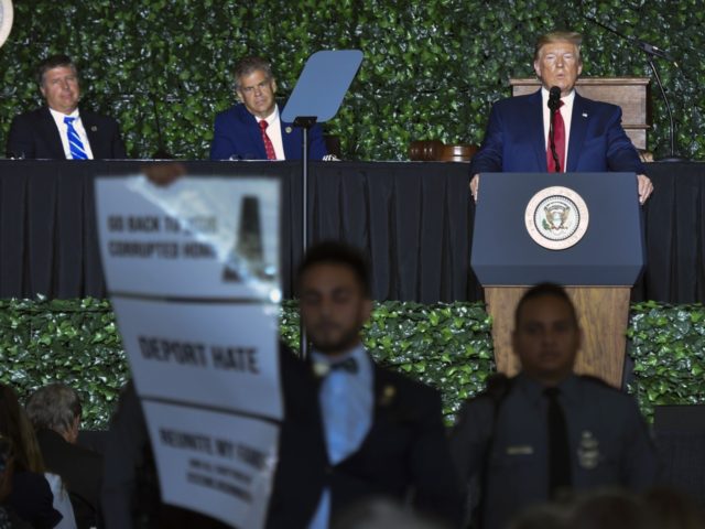 A protester holds a sign as US President Donald Trump speaks during an event commemorating