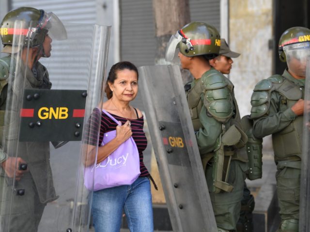 A woman walks by as members of Venezuela's Bolivarian National Guard block stand guard in