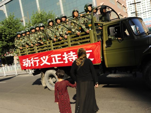 A Muslim ethnic Uighur woman and her daughter try to cross the road as Chinese paramilitar