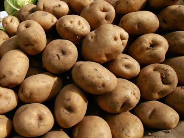 A vegetable vendor waits for customers behind a stack of potatoes at a market in Beijing,