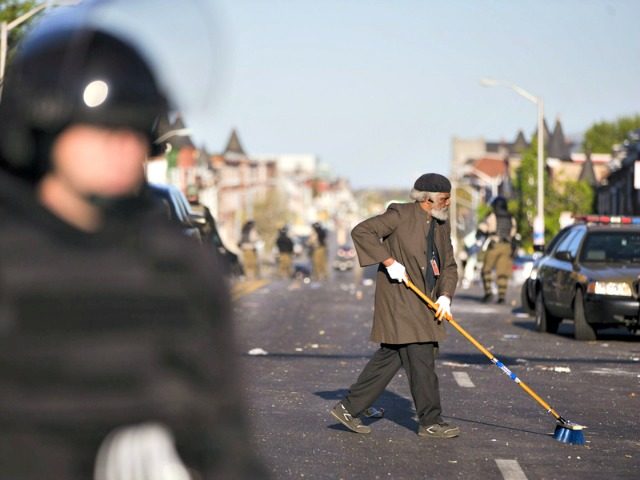 Residents clean streets as law enforcement officers stand guard, in Baltimore, in the afte