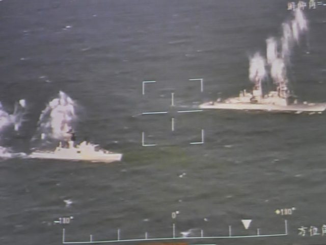 Warships launching countermeasures are seen on a screen showing a real-time feed from an i