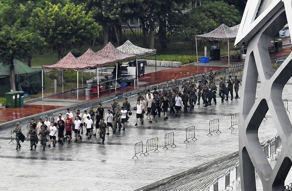 This Friday, Aug. 16, 2019, photo shows members of China's paramilitary People's Armed Police, in military fatigues and T-shirts, outside Shenzhen Bay Stadium in Shenzhen, China. Chinese police marched and practiced crowd control tactics at the sports complex in Shenzhen across from Hong Kong on Friday, in what some interpreted as a threat against pro-democracy protesters in the semiautonomous territory.(Madoka Ikegami/Kyodo News via AP)