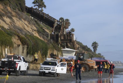 Lifeguards and search and rescue personnel work at the site of a cliff collapse at a popul