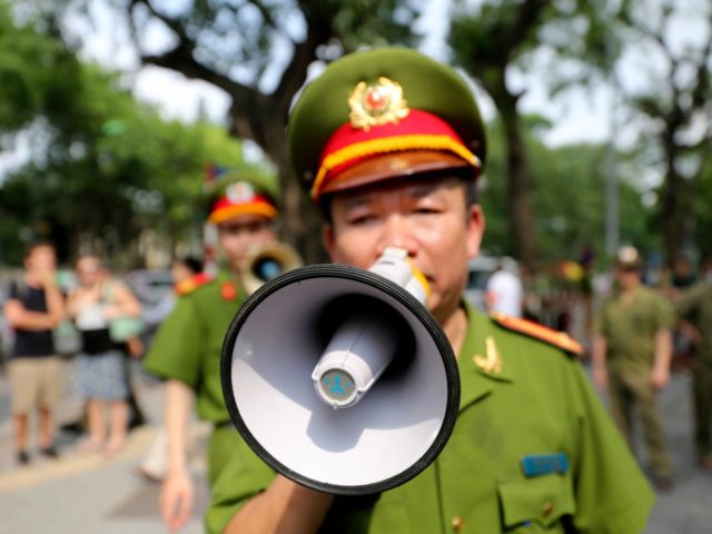 A Vietnamese police officer uses a speaker to order pedestrians including journalists to l