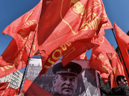 TOPSHOT - A Russian Communist party activist holds a red flag as he stands next to a banne