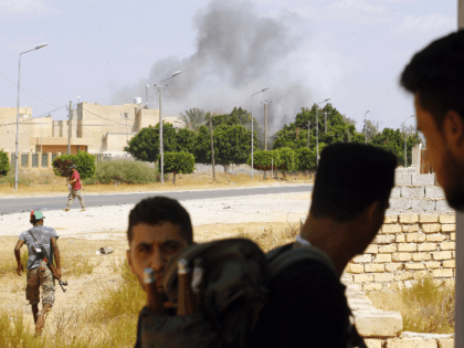 A plume of smoke rises above buildings as fighters loyal to the internationally-recognised Government of National Accord (GNA) gather during clashes with forces loyal to strongman Khalifa Haftar, in Espiaa, about 40 kilometers (25 miles) south of the Libyan capital Tripoli on August 21, 2019. (Photo by Mahmud TURKIA / …