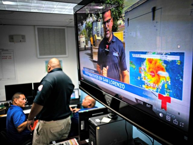 Emergency Center personnel stand next to a tv screen showing a meteorological image of the