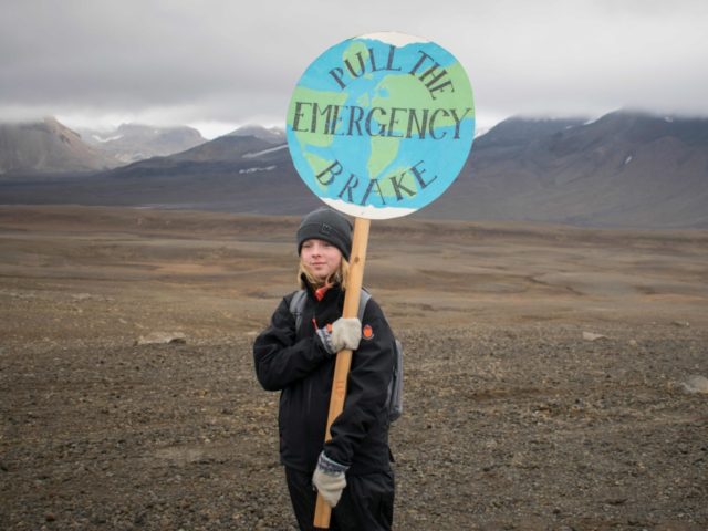 TOPSHOT - An Icelandic girl poses for a photo with a "Pull the emergency brake" sign near to where a monument was unveiled at the site of Okjokull, Iceland's first glacier lost to climate change in the west of Iceland on August 18, 2019. (Photo by Jeremie RICHARD / AFP) …