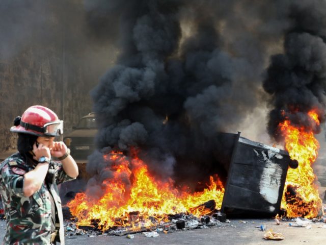A Lebanese firefighter walks past a burning dumpster during a demonstration in central Bei
