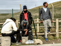 Migrants sit under the winter sun close to their make shift camp in the vicinity of the former 'Jungle' camp site, near the northern French port city of Calais on February 18, 2019. - Between 2015 and 2016 some 10,00 migrants lived in an informal camp which became know as …