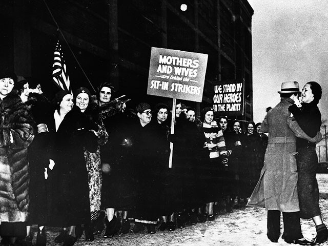 Daily parades of members of the emergency brigade composed of wives, sisters and sweethearts of sit-down strikers, feature outdoor demonstrations at plant in Flint, Michigan, Feb. 5, 1937. Here part of a march staged during a snowstorm with one couple adding impromptu entertainment. (AP Photo)