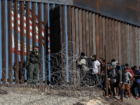 Central American migrants look through a border fence as a US Border PatRol agents stands guard near the El Chaparral border crossing in Tijuana, Baja California State, Mexico, on November 25, 2018. - Hundreds of migrants attempted to storm a border fence separating Mexico from the US on Sunday amid …