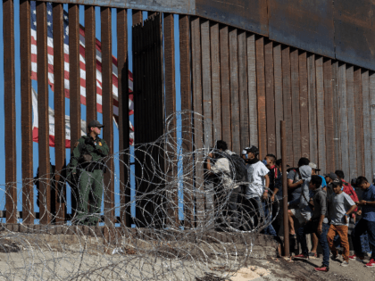 Central American migrants look through a border fence as a US Border PatRol agents stands