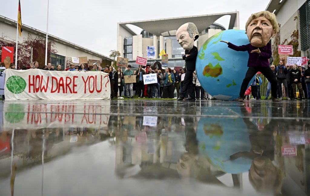 TOPSHOT - Environmentalists hold a banner reading "How dare you", quoting Swedish teenage climate activist Greta Thunberg, and wear masks of German Chancellor Angela Merkel and Finance Minister and Vice-Chancellor Olaf Scholz as they protest outside the German Chancellery where is taking place the weekly cabinet meeting in Berlin on September 25, 2019. (Photo by Tobias SCHWARZ / AFP) (Photo credit should read TOBIAS SCHWARZ/AFP/Getty Images)