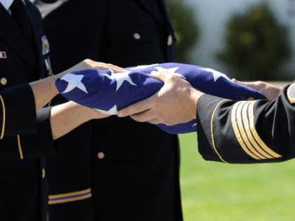 Officers Of A Military Honor Guard carefully prepare a flag that graced the casket of one