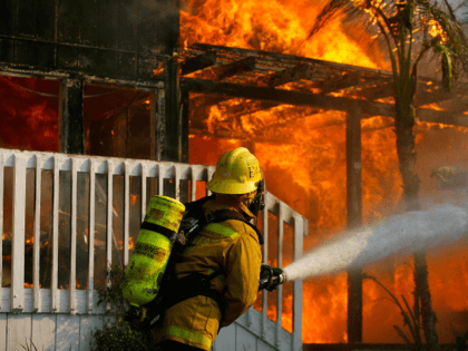 A US forestry firefighter cools a burning modular home to protect a nearby structure in De