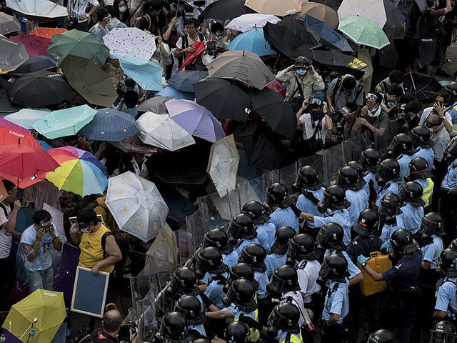 Pro-democracy protesters hold umbrellas and wear protective clothing in front of a police