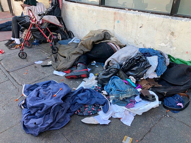 In this photo taken July 25, 2019, sleeping people, discarded clothes and used needles sit