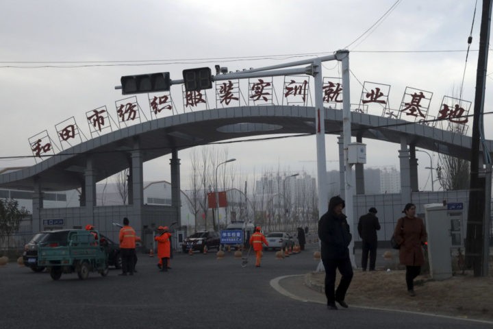 In this Wednesday, Dec. 5, 2018, photo, residents pass by the entrance to the "Hotan City apparel employment training base" where Hetian Taida has a factory in Hotan in western China's Xinjiang region. This is one of a growing number of internment camps in the Xinjiang region, where by some estimates 1 million Muslims are detained, forced to give up their language and their religion and subject to political indoctrination. Now, the Chinese government is also forcing some detainees to work in manufacturing and food industries. Some of them are within the internment camps; others are privately owned, state-subsidized factories where detainees are sent once they are released. (AP Photo/Ng Han Guan)