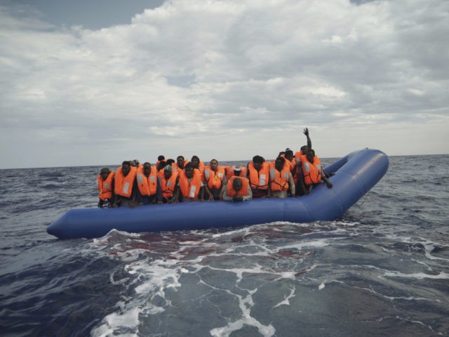 A migrant waves his hand in the air from on a blue rubber boat some 14 nautical miles from