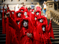 TOPSHOT - Extinction Rebellion climate change activists in red costume attend a mass "die in" in the main hall of the Natural History Museum in London on April 22, 2019, on the eighth day of the environmental group's protest calling for political change to combat climate change. - Climate change …