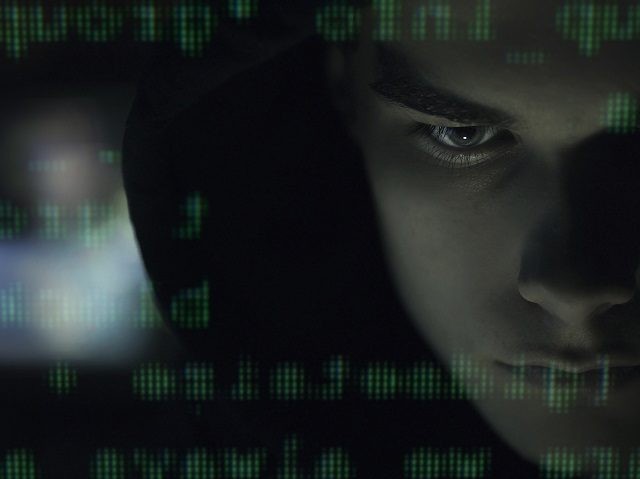 Cool young hacker with hoodie posing in the dark and programming code, cyber security and development concept