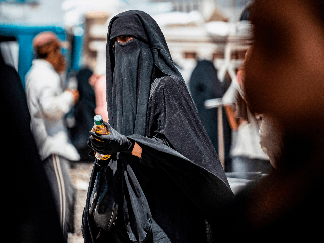 A woman wearing a niqab (full face veil) holds a bottle of sunflower oil distributed as part of food aid at al-Hol camp for displaced people in al-Hasakeh governorate in northeastern Syria on July 22, 2019, as people collect UN-provided humanitarian aid packages. (Photo by Delil souleiman / AFP) (Photo …